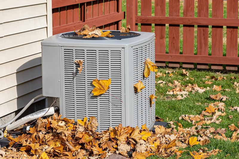 Dirty air conditioning unit cover in leaves during autumn. Home air conditioning, hvac, repair, service, fall cleaning and maintenance.