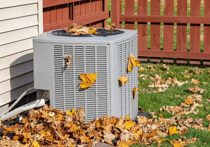 Dirty air conditioning unit cover in leaves during autumn. Home air conditioning, hvac, repair, service, fall cleaning and maintenance.